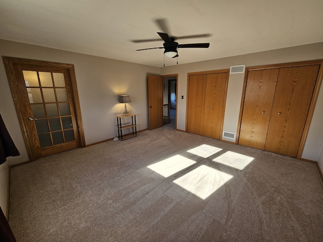 unfurnished bedroom with two closets, light colored carpet, and ceiling fan