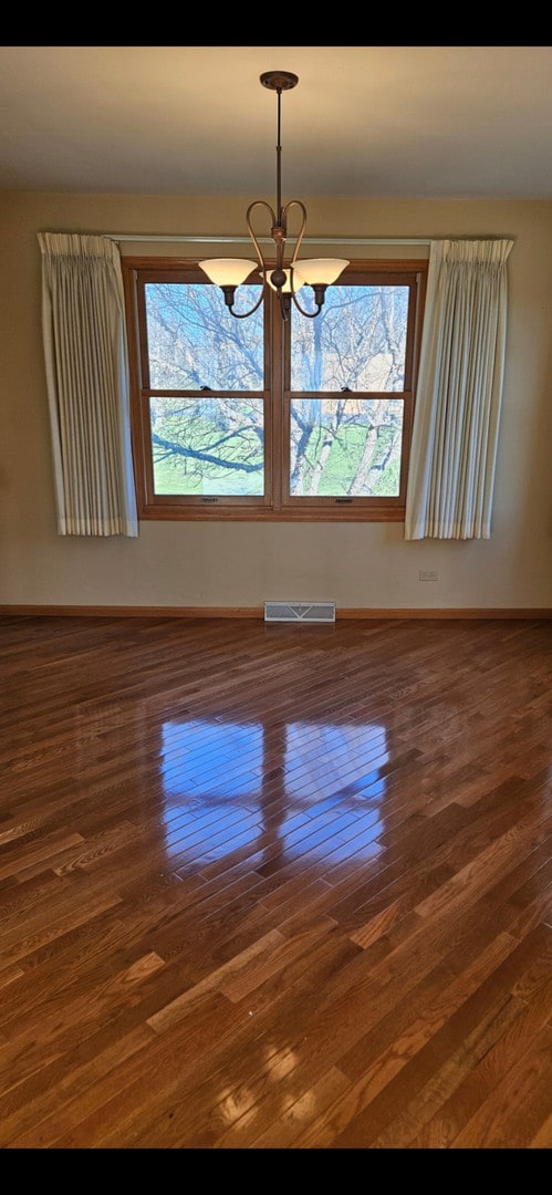 unfurnished room with a wealth of natural light, dark hardwood / wood-style flooring, and an inviting chandelier