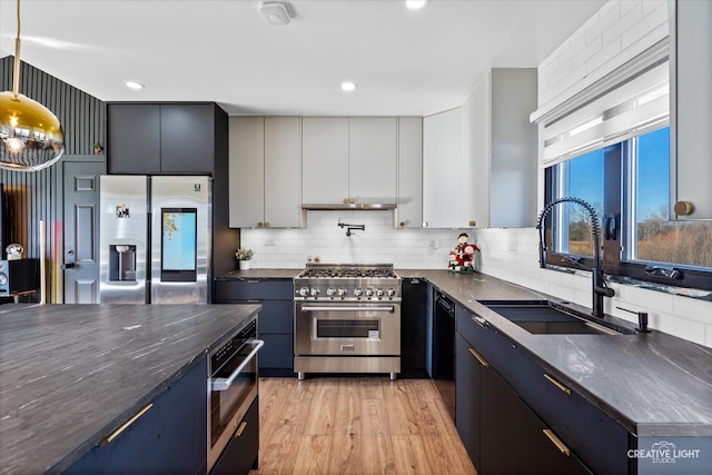 kitchen featuring appliances with stainless steel finishes, light wood-type flooring, tasteful backsplash, sink, and decorative light fixtures