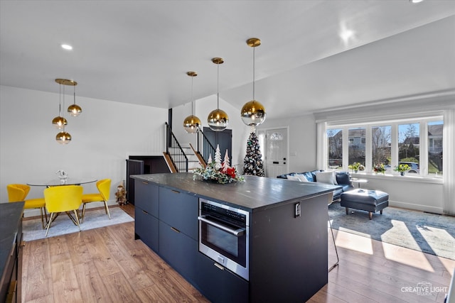 kitchen with decorative light fixtures, stainless steel oven, a kitchen island, and light wood-type flooring