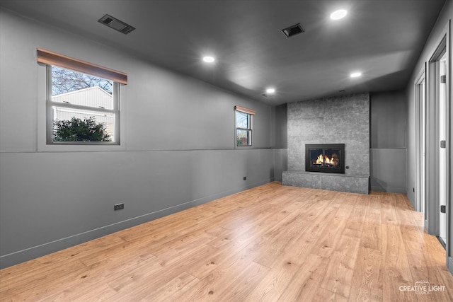 unfurnished living room featuring light wood-type flooring, a wealth of natural light, and a tiled fireplace