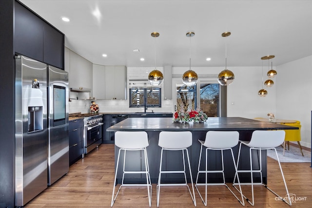 kitchen with light wood-type flooring, high end appliances, sink, blue cabinetry, and decorative light fixtures