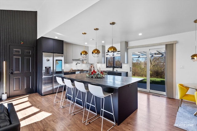 kitchen with built in fridge, backsplash, light wood-type flooring, and hanging light fixtures