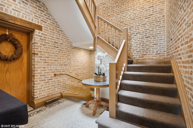 stairway with carpet flooring, a towering ceiling, and brick wall