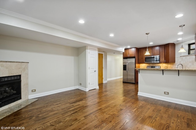 kitchen with light stone countertops, stainless steel appliances, dark hardwood / wood-style flooring, kitchen peninsula, and a breakfast bar area