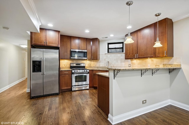 kitchen featuring a breakfast bar, appliances with stainless steel finishes, decorative light fixtures, and dark wood-type flooring