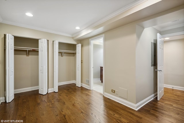 unfurnished bedroom with dark hardwood / wood-style flooring, electric panel, crown molding, and multiple closets