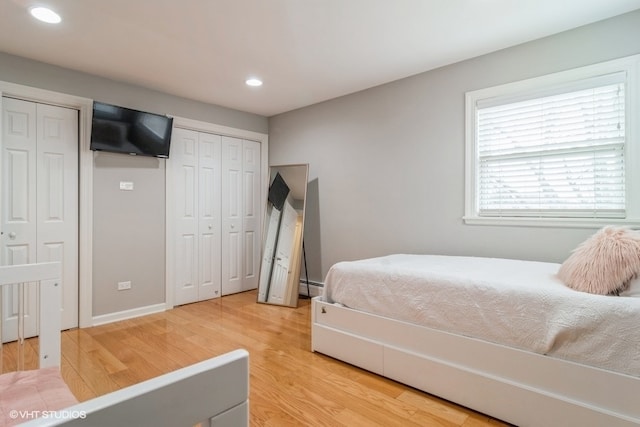 bedroom featuring hardwood / wood-style flooring, multiple closets, and a baseboard heating unit