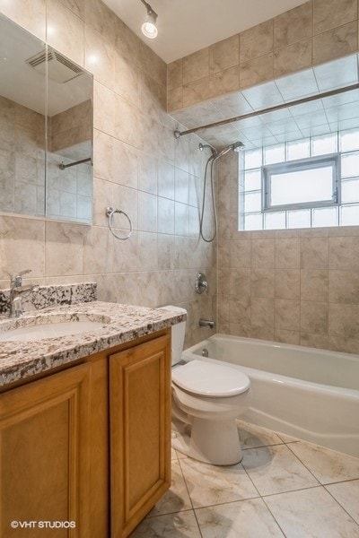 full bathroom featuring vanity, tiled shower / bath combo, tile walls, and toilet