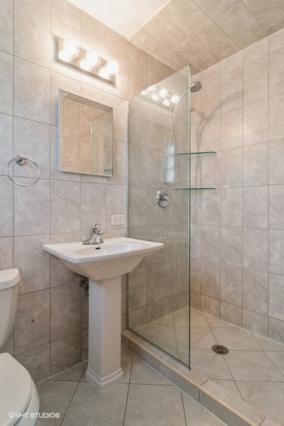 bathroom with tiled shower, tile patterned floors, tile walls, and toilet