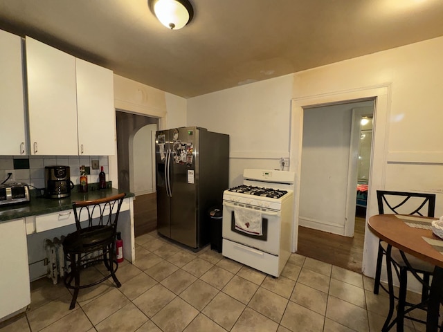 kitchen with backsplash, white cabinets, stainless steel fridge, light wood-type flooring, and white gas range