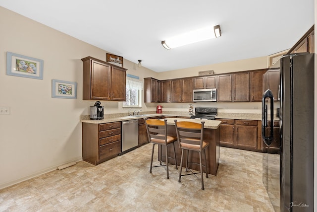 kitchen with a kitchen bar, light stone countertops, dark brown cabinets, black appliances, and a kitchen island