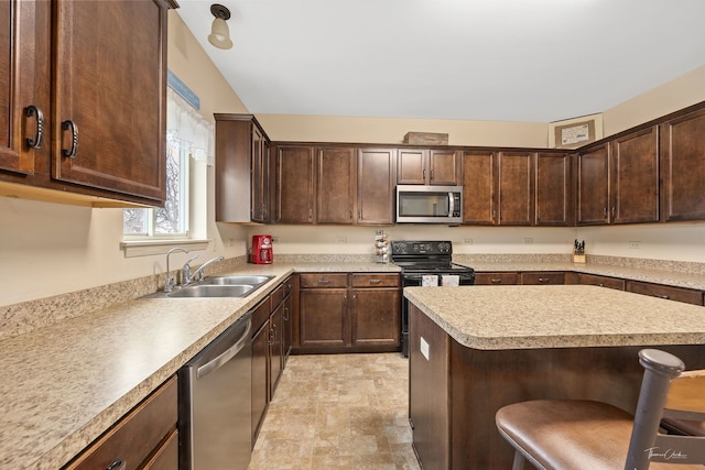 kitchen with a kitchen bar, dark brown cabinetry, sink, and appliances with stainless steel finishes