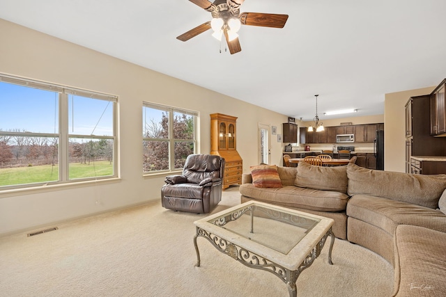 carpeted living room with ceiling fan with notable chandelier