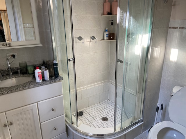 bathroom featuring vanity, toilet, a shower with door, and tile walls