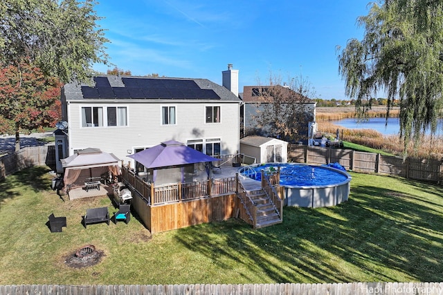 back of property with a gazebo, a pool side deck with water view, a lawn, and a shed