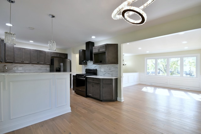 kitchen with black stove, wall chimney exhaust hood, dark brown cabinetry, light hardwood / wood-style floors, and stainless steel fridge with ice dispenser