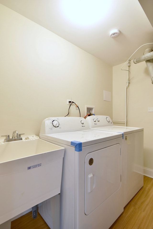 laundry area with washing machine and dryer, sink, and light wood-type flooring