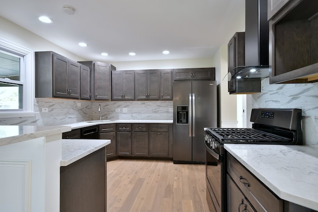 kitchen featuring stainless steel appliances, tasteful backsplash, light stone counters, light hardwood / wood-style floors, and dark brown cabinets