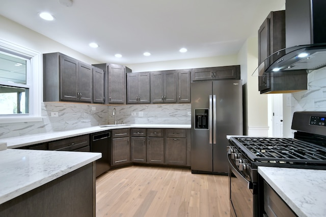 kitchen featuring sink, wall chimney exhaust hood, light wood-type flooring, tasteful backsplash, and stainless steel appliances