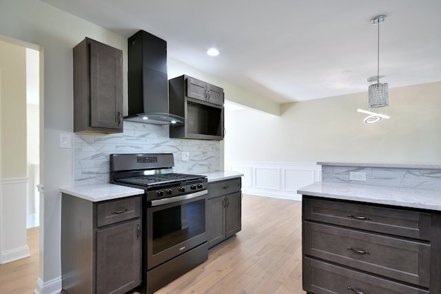 kitchen featuring light hardwood / wood-style flooring, wall chimney exhaust hood, light stone countertops, decorative light fixtures, and stainless steel range with gas stovetop