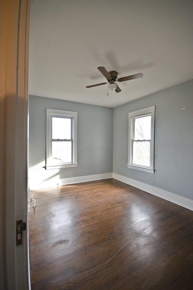 empty room with a wealth of natural light, dark wood-type flooring, and ceiling fan