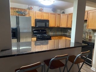 kitchen with kitchen peninsula, light wood-type flooring, backsplash, black appliances, and a breakfast bar area