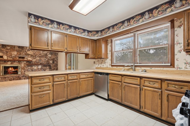 kitchen featuring kitchen peninsula, light carpet, stainless steel dishwasher, sink, and a stone fireplace