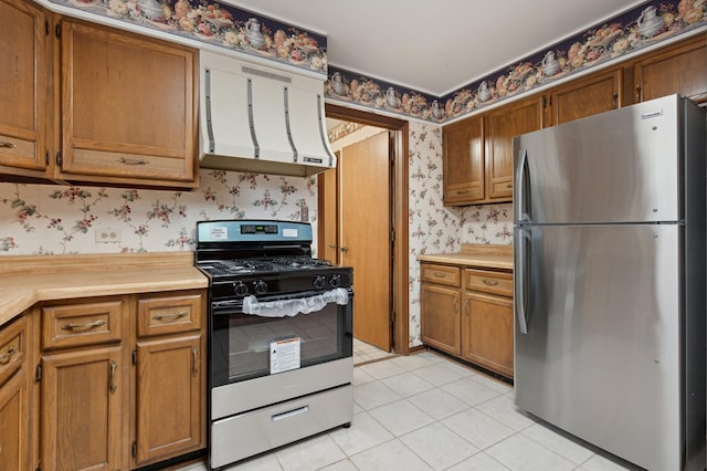 kitchen with stainless steel fridge, range hood, light tile patterned floors, and range with gas stovetop