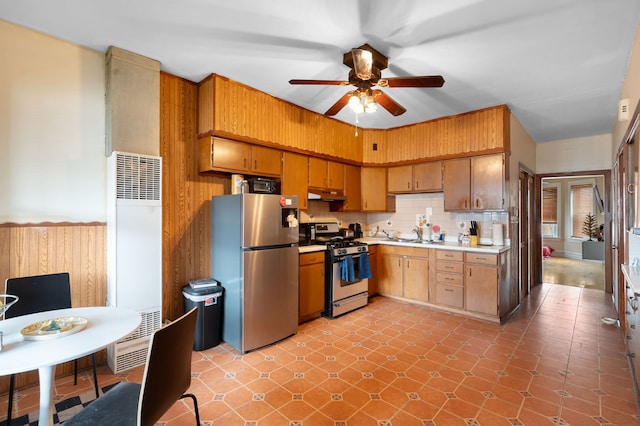 kitchen with sink, appliances with stainless steel finishes, wooden walls, ceiling fan, and decorative backsplash