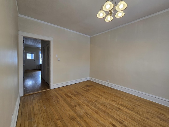 empty room with wood-type flooring, a chandelier, and crown molding