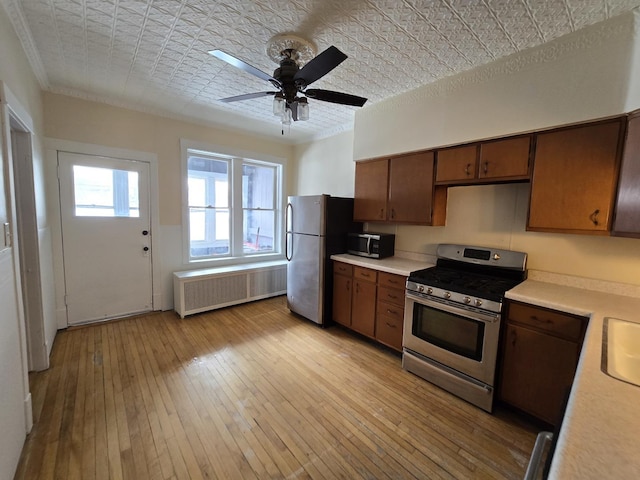 kitchen featuring light wood-type flooring, ornamental molding, radiator heating unit, ceiling fan, and stainless steel appliances