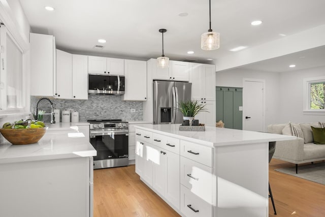 kitchen featuring appliances with stainless steel finishes, light wood-type flooring, white cabinets, a kitchen island, and hanging light fixtures