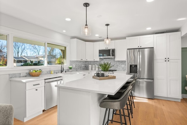 kitchen featuring sink, a center island, stainless steel appliances, light hardwood / wood-style floors, and white cabinets