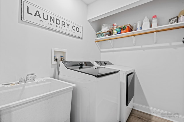 clothes washing area featuring washing machine and dryer, sink, and hardwood / wood-style flooring