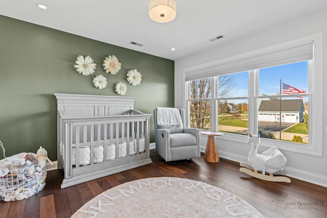 bedroom with a crib and dark wood-type flooring