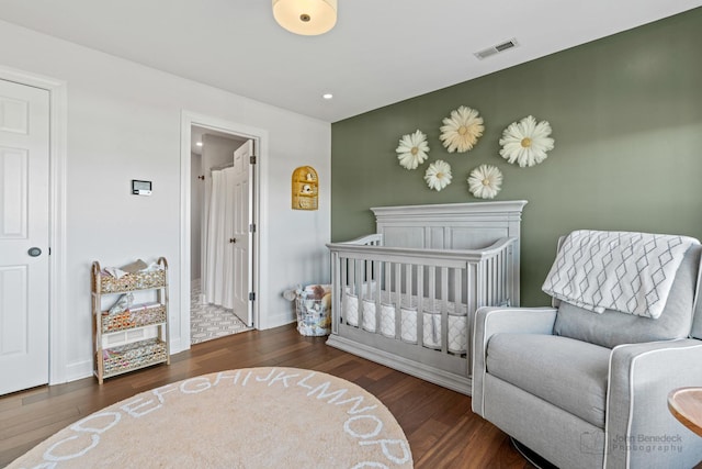 bedroom with dark hardwood / wood-style floors and a nursery area