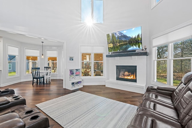 living room with a brick fireplace, a wealth of natural light, and dark wood-type flooring