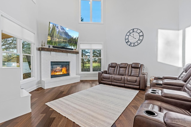 living room with dark hardwood / wood-style flooring, a towering ceiling, and a brick fireplace