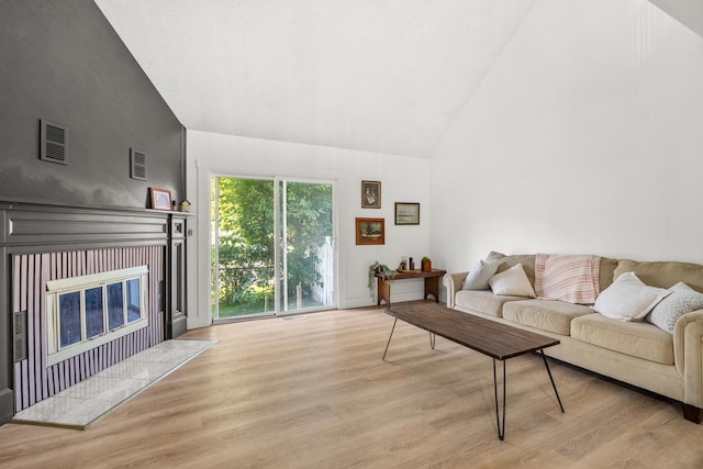 living room featuring a tile fireplace, high vaulted ceiling, and light wood-type flooring