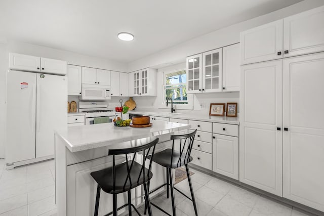 kitchen with sink, white cabinets, a kitchen breakfast bar, a center island, and white appliances