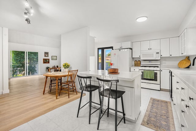 kitchen with white appliances, a breakfast bar, white cabinets, a kitchen island, and light wood-type flooring