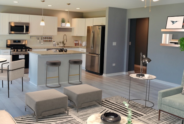 kitchen with sink, light wood-type flooring, an island with sink, white cabinetry, and stainless steel appliances