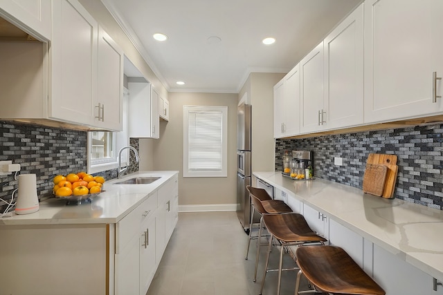 kitchen with backsplash, a kitchen bar, white cabinetry, and sink