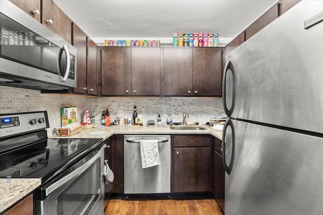 kitchen with sink, appliances with stainless steel finishes, dark brown cabinets, light hardwood / wood-style floors, and light stone counters