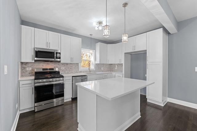 kitchen with appliances with stainless steel finishes, dark hardwood / wood-style flooring, sink, white cabinets, and a kitchen island