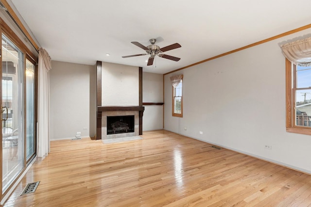 unfurnished living room featuring light hardwood / wood-style floors, crown molding, a wealth of natural light, and a tiled fireplace