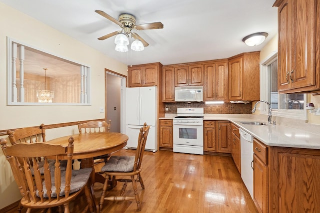 kitchen featuring sink, light hardwood / wood-style flooring, decorative light fixtures, white appliances, and ceiling fan with notable chandelier