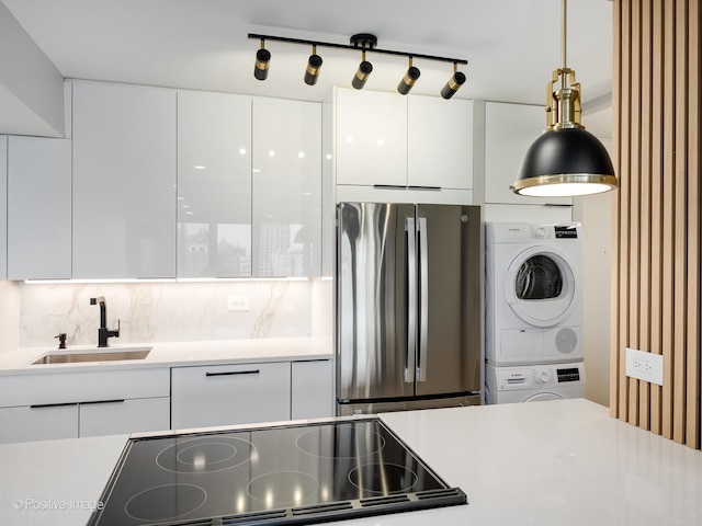 kitchen featuring stacked washing maching and dryer, sink, decorative light fixtures, white cabinetry, and stainless steel refrigerator