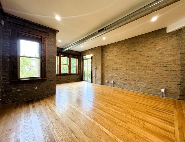 unfurnished room with brick wall, wood-type flooring, and a wealth of natural light